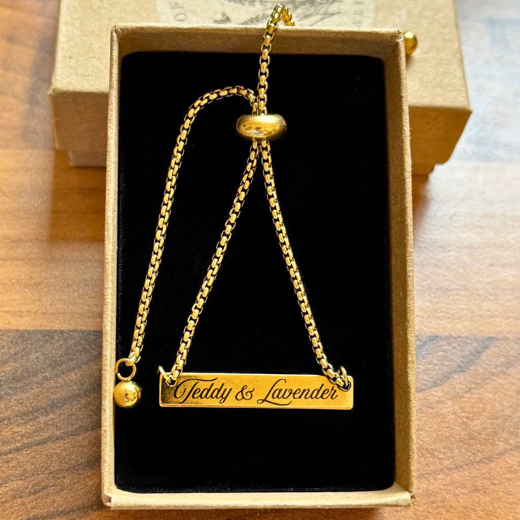 Adjustable gold colour bracelet with  Teddy and Lavender engraved on the bar of the bracelet in a brown box.
