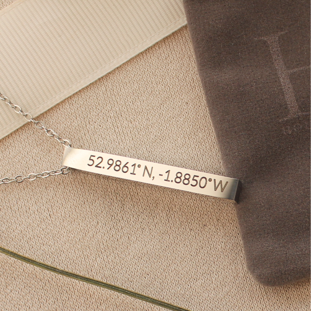 A silver bar necklace engraved with geographic coordinates '52.9861° N, -1.